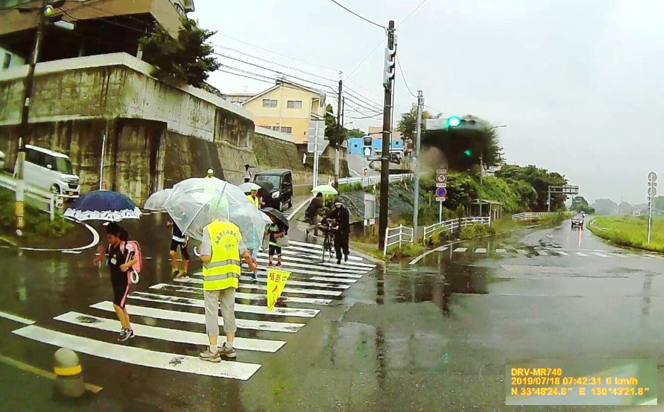 雨の中、大辻町信号、七重町入口の横断歩道を渡る子どもたちの写真
