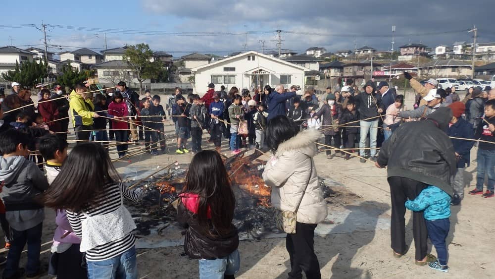 子どもたちや地域の方が竹さおの先に餅をつるし焼いている写真